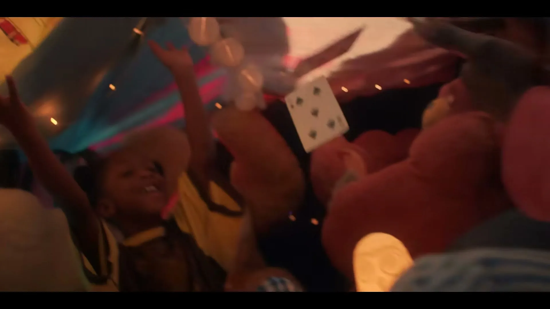 A child in a blanket fort throws playing cards into the air, surrounded by pillows and string lights, in a playful moment.