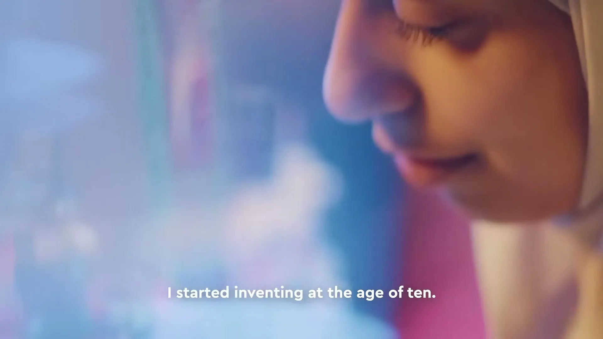 A young girl in a hijab looks down at a colorful Lego creation, with a soft, dreamy focus on her face and the toy.