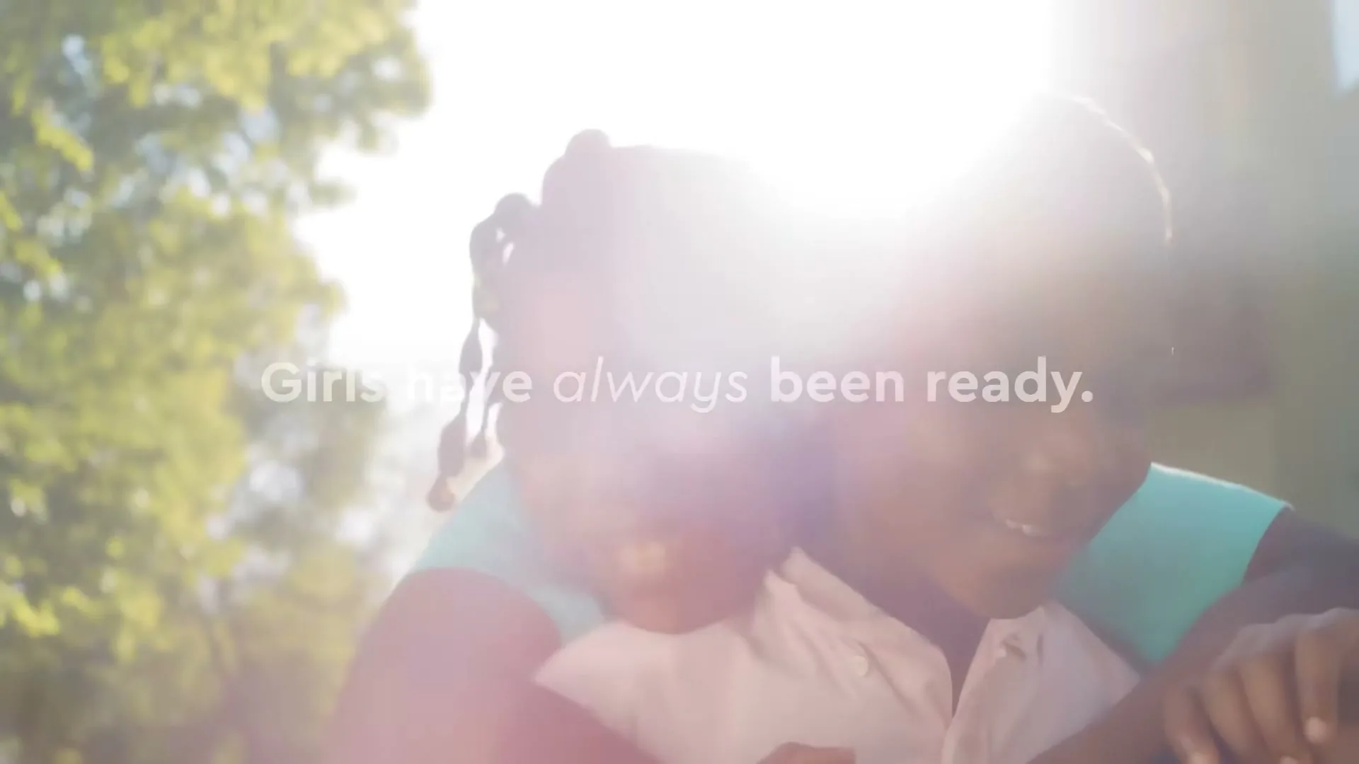 Two young Black children, a boy and a girl, embrace and smile in bright sunlight outdoors, with text overlay.