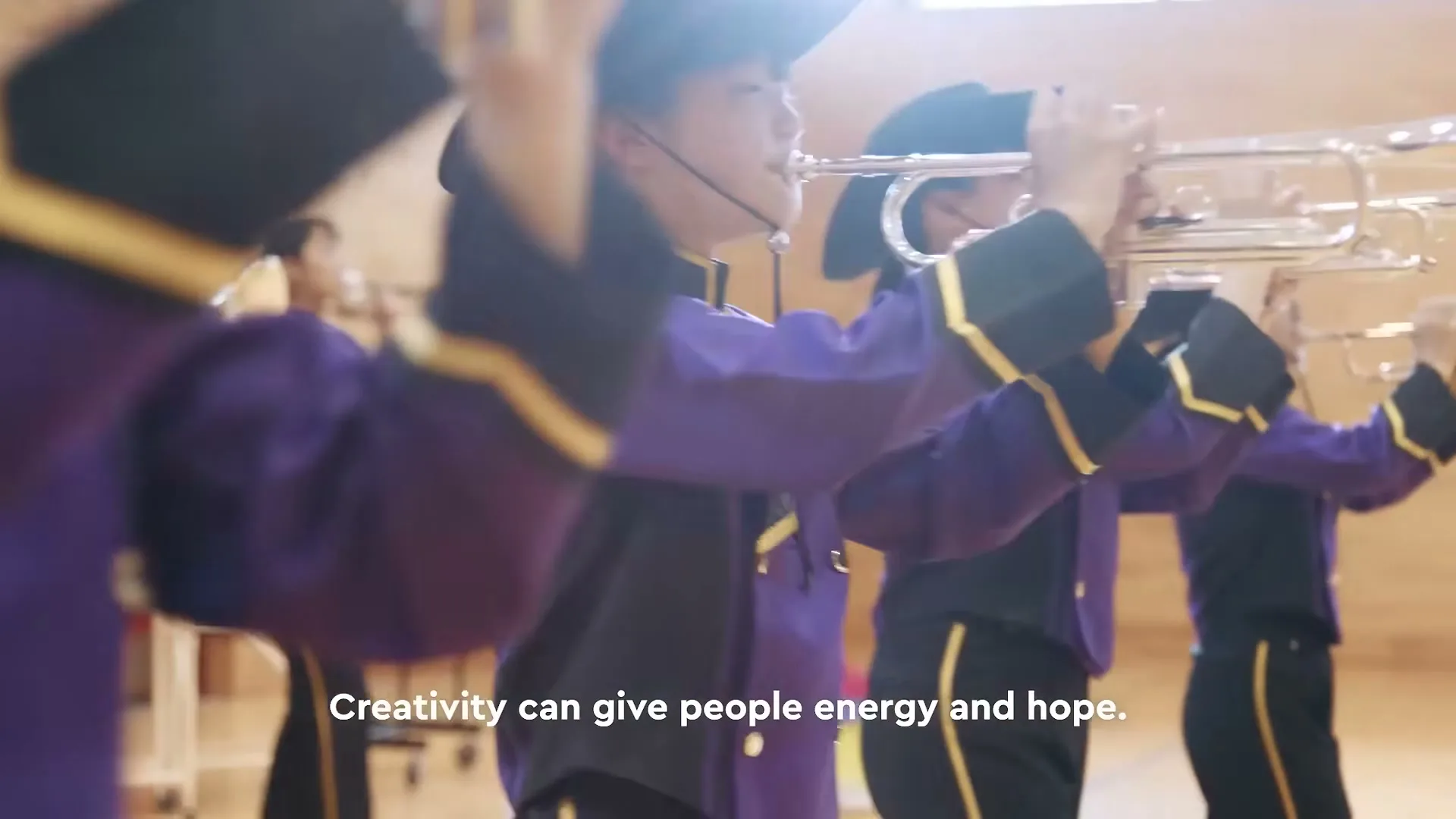 A group of young musicians in purple and black uniforms with cowboy hats play trumpets in a brightly lit room.
