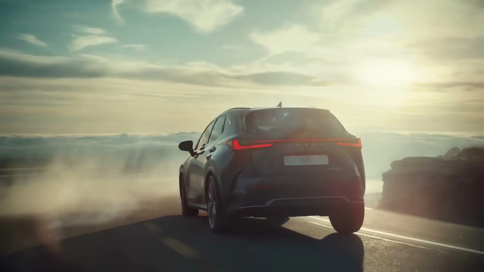 A dark grey Lexus NX drives away on a mountain road above the clouds, with the sun setting in the background.