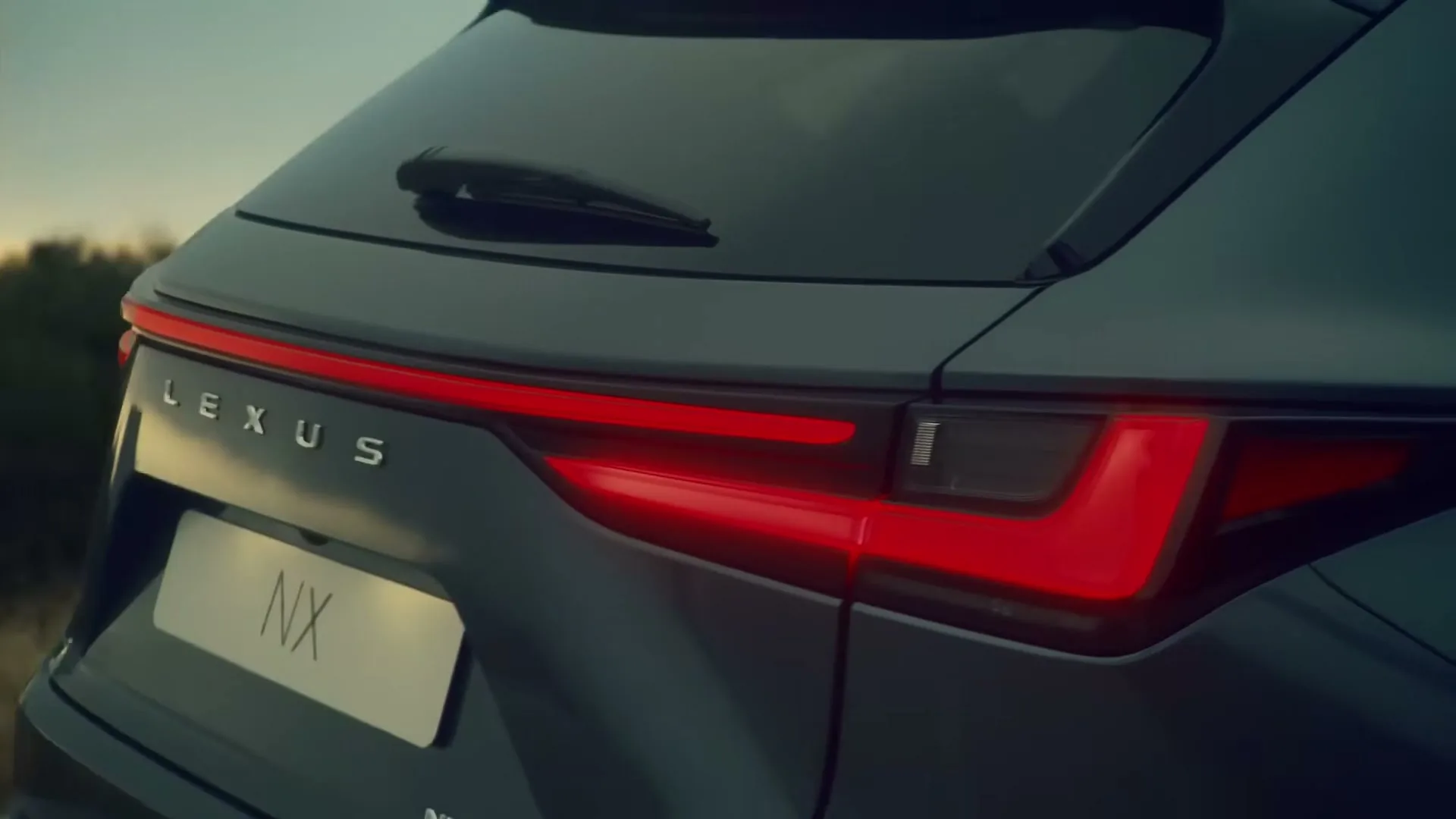 A close-up shot of the rear of a dark grey Lexus NX SUV, with its red taillights illuminated, parked outdoors at dusk.