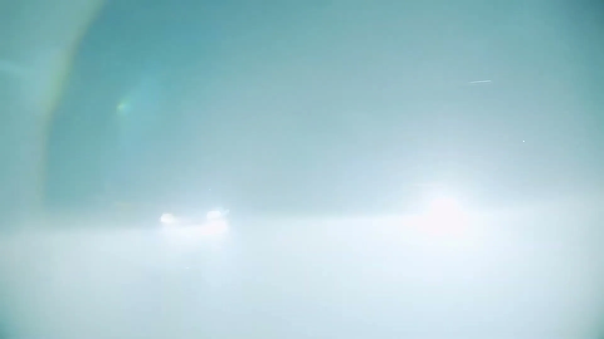 Two cars, one black and one red, are driving fast on a road at night, with bright headlights creating a hazy, blurry effect.