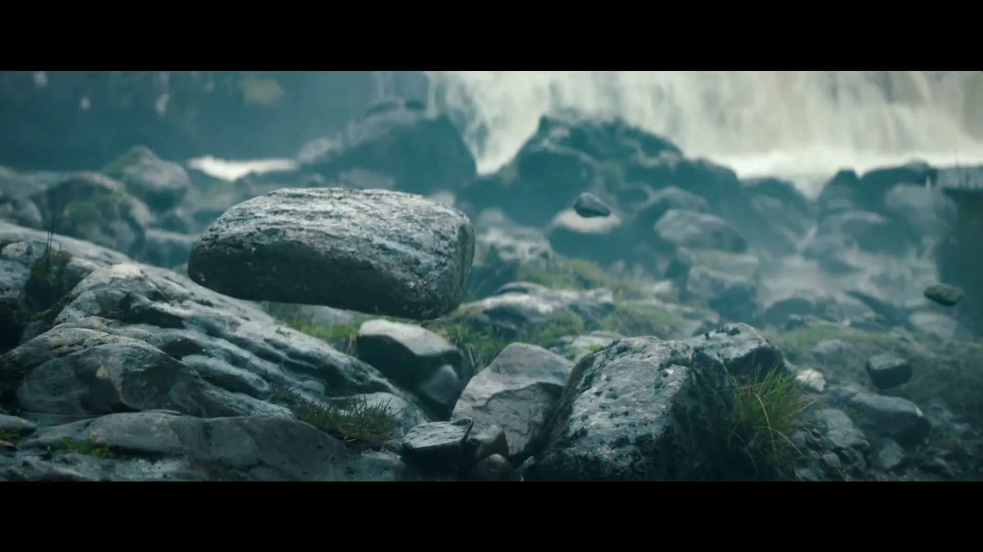 A large, wet rock floats above a rocky, mossy landscape with a blurred waterfall in the background, as other smaller rocks also float around it.
