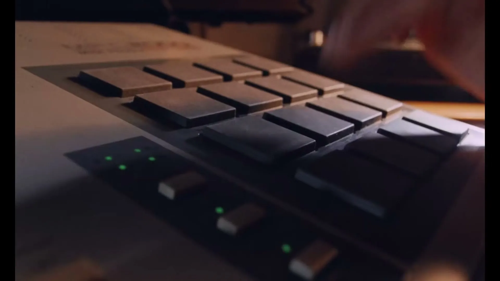 A person's hand quickly presses buttons on a vintage drum machine, with green indicator lights visible on the device.