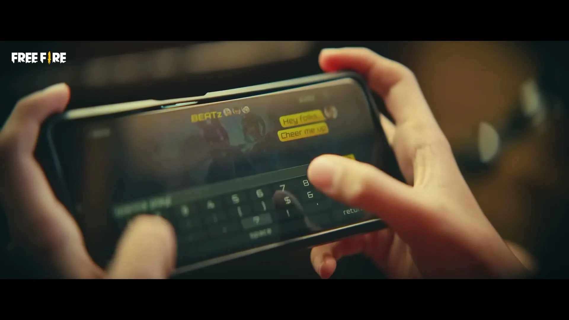 A close-up shot shows a person's hands holding a smartphone horizontally, typing a message on the screen, with a game interface visible in the background.