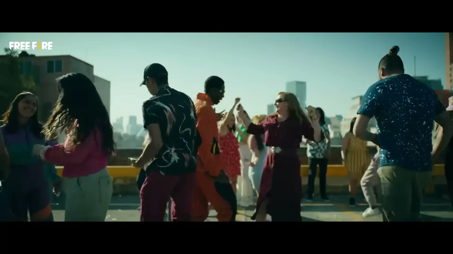 A diverse group of people dance on a rooftop, with a woman in a green shirt playing a mobile game on her phone.