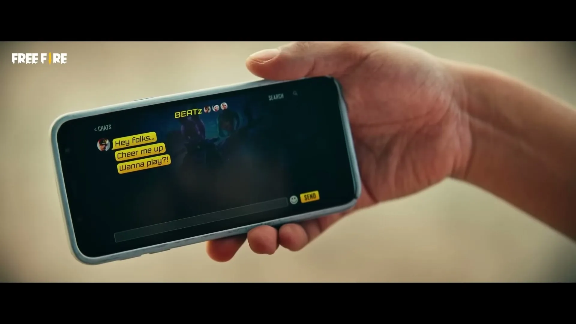 A person's hand holds a smartphone displaying a chat interface with messages like "Hey Folks... Cheer me up Wanna play?" on a blurred background.