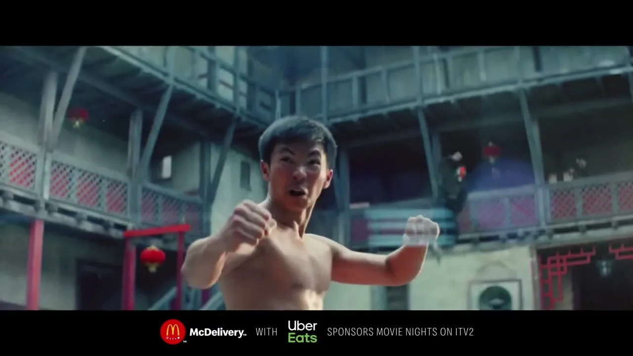 A shirtless young man with short dark hair, resembling Bruce Lee, practices martial arts in a traditional Chinese courtyard.
