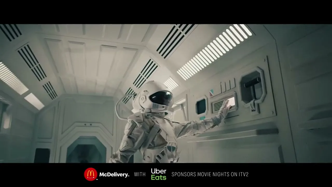 An astronaut in a white suit presses a button on a control panel inside a futuristic spaceship, causing red lights to flash.