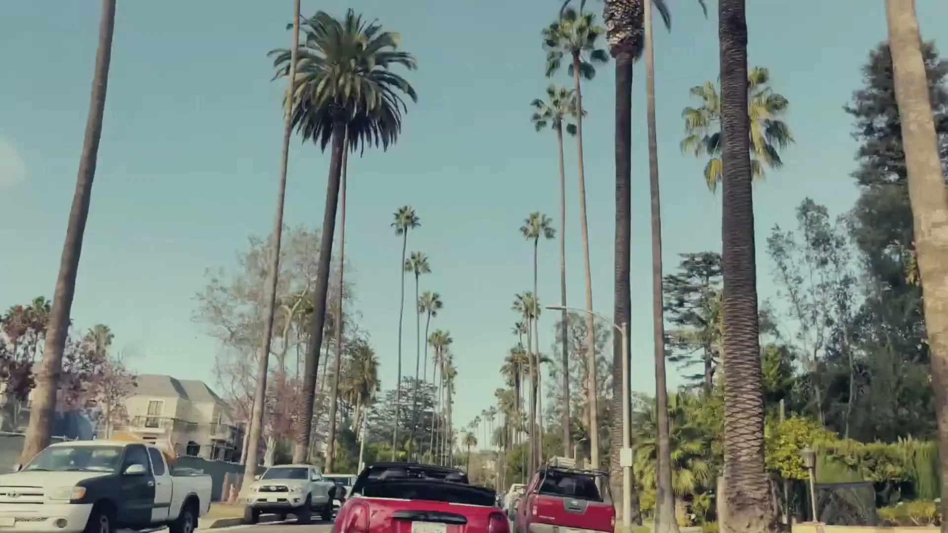 A red Mini Cooper convertible drives down a palm tree-lined street in a suburban neighborhood on a sunny day.