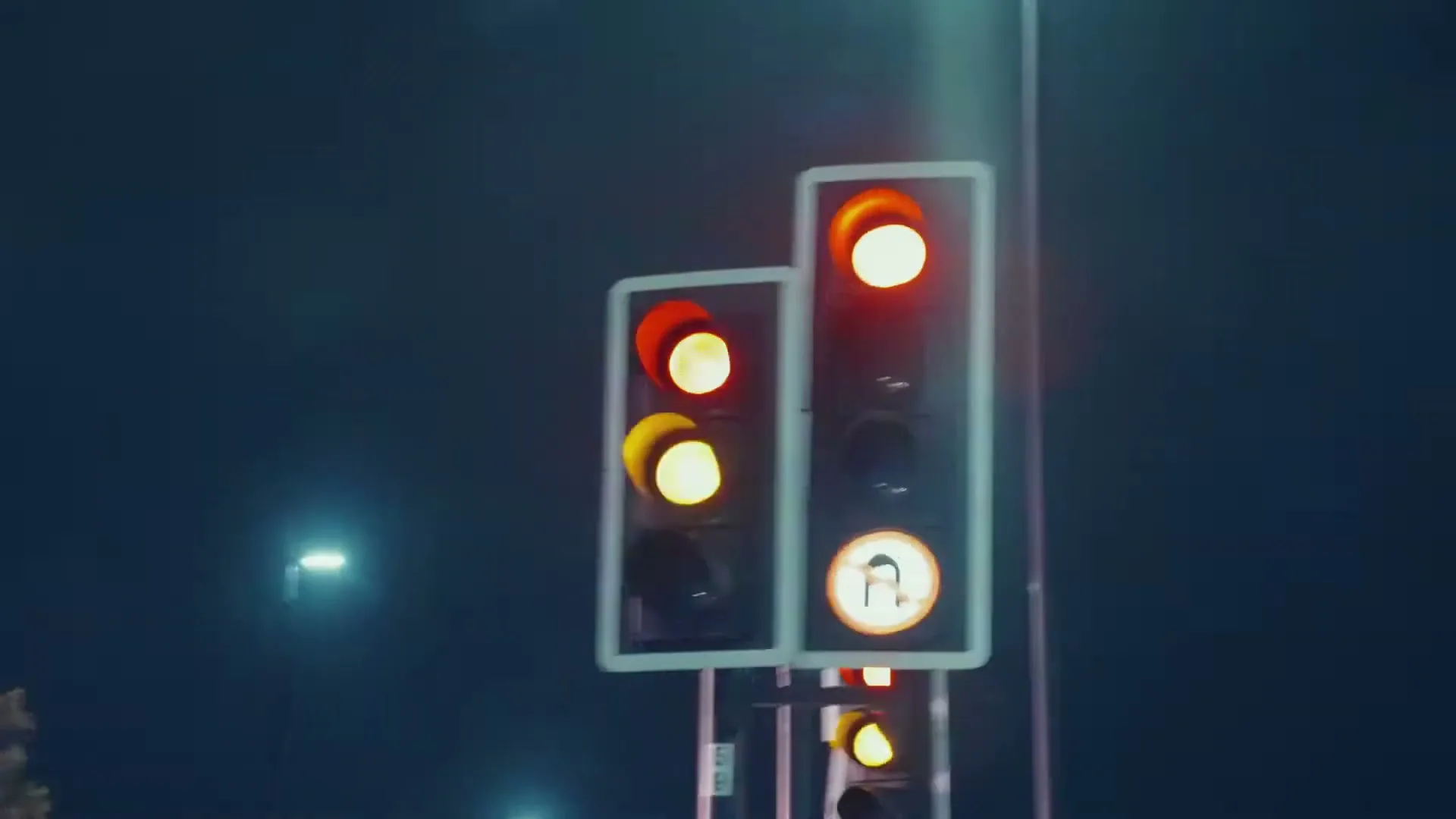 A blurry shot of traffic lights at night, with red and yellow lights visible, as the camera quickly pans to the right.