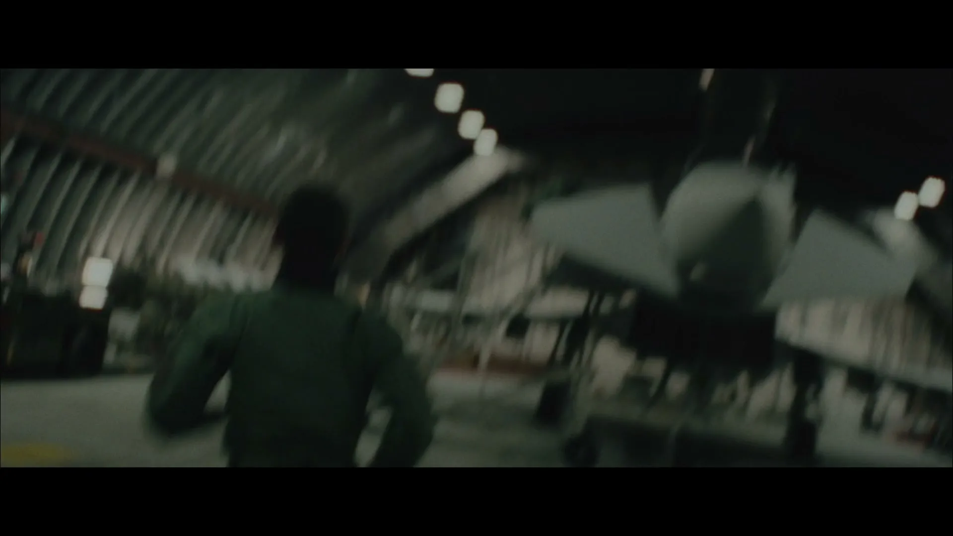 Two men in military uniforms look at screens in a dark control room, then a pilot runs towards a fighter jet in a hangar, and finally a fighter jet takes off at night.