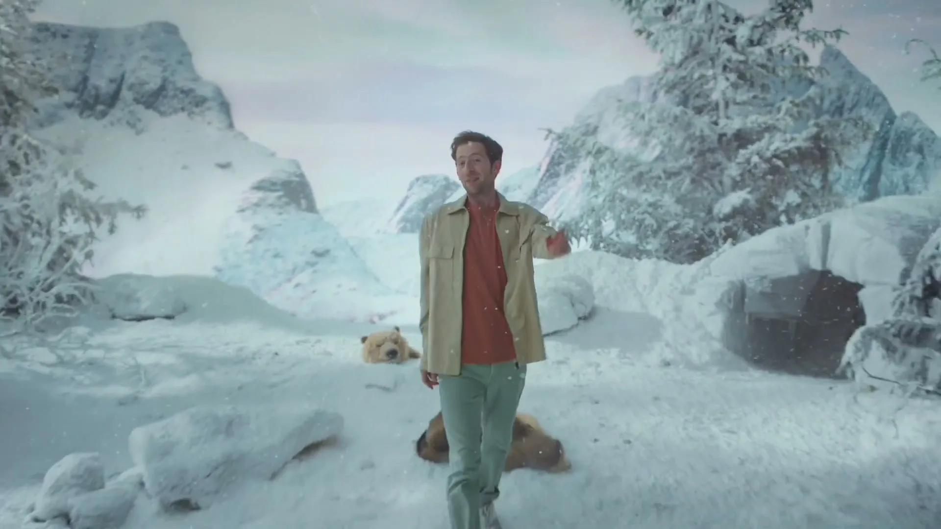 A man in a fur coat, then a jacket, walks and talks in a snowy, mountainous landscape with a bear rug.