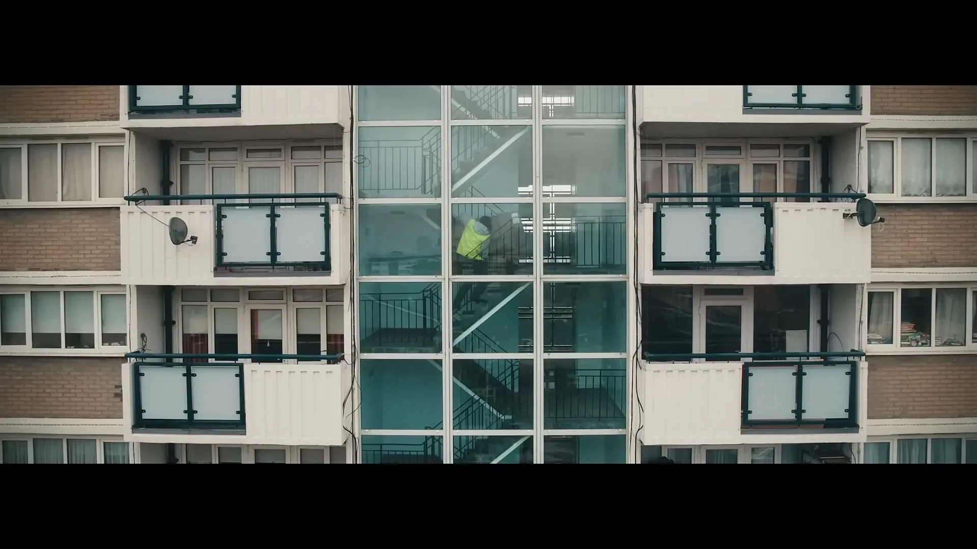 A man in a high-vis jacket walks up the stairs of a residential building with a glass exterior staircase.