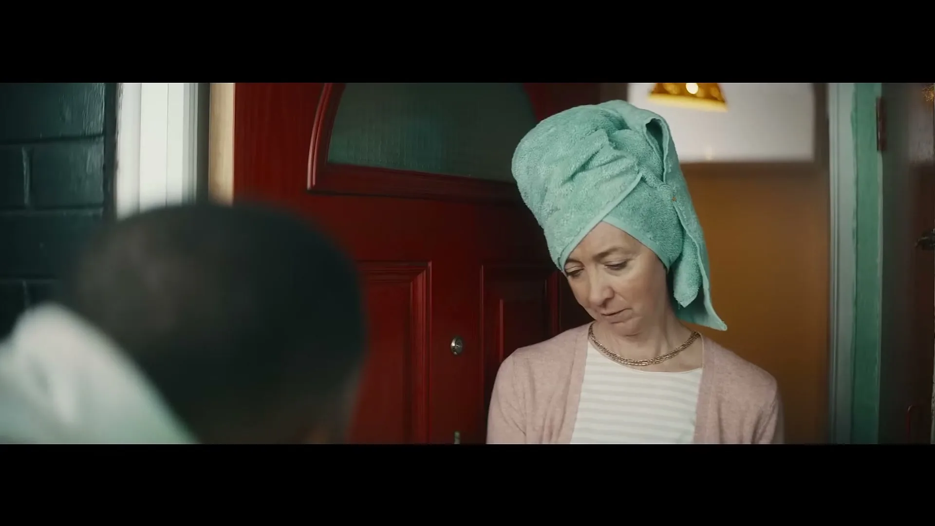 A woman with a towel on her head looks confused while talking to a delivery person at her front door.
