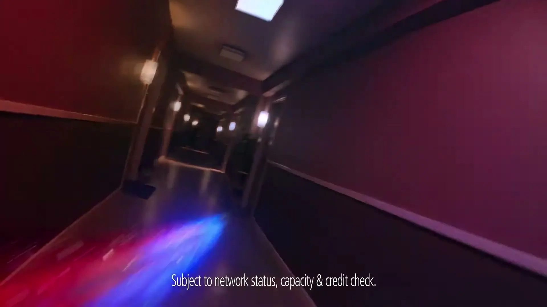 A wide-angle shot shows a long, dark hallway with doors and wall sconces, as red and blue light trails streak across the floor, creating a sense of speed.