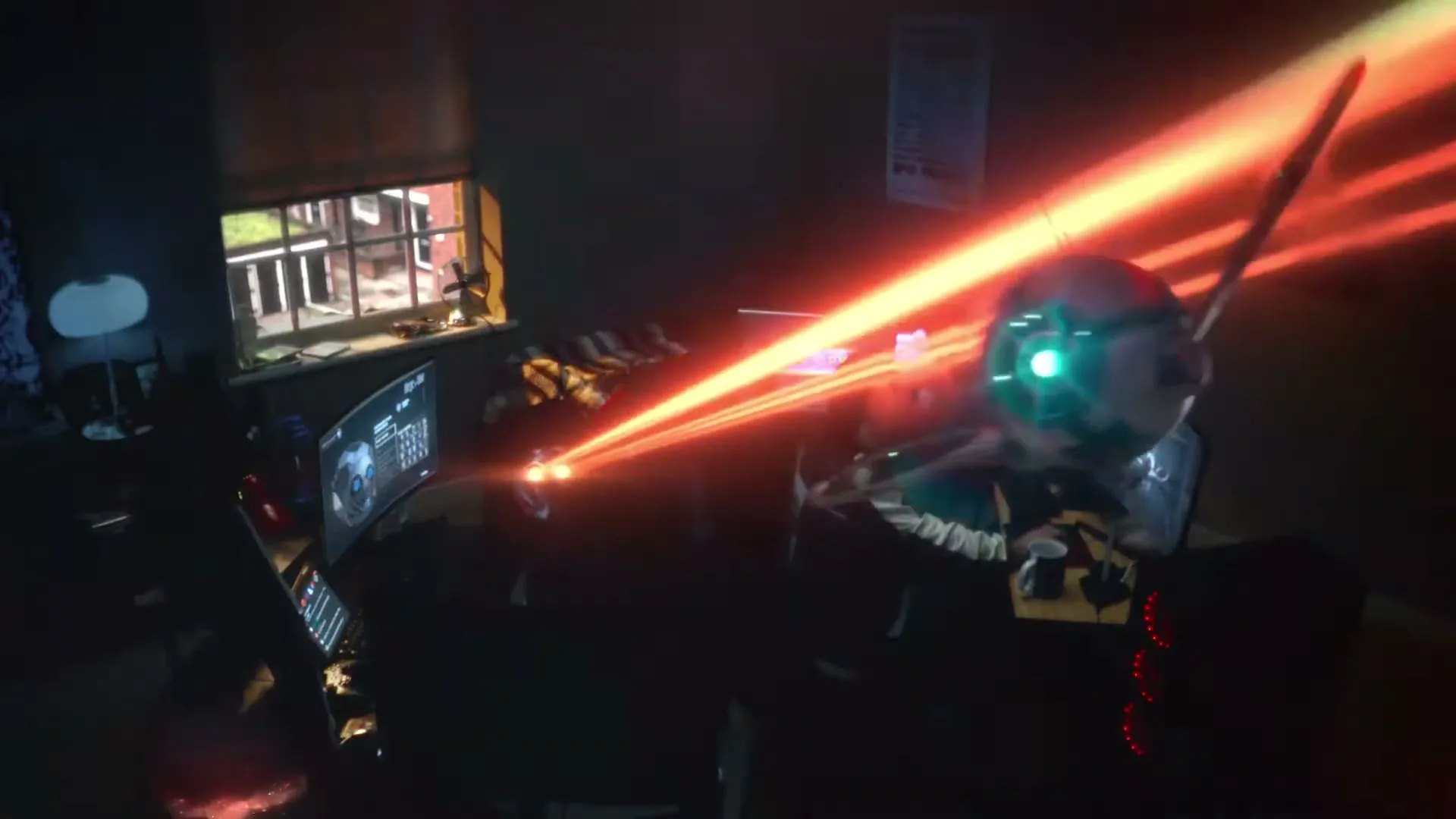 A young man in a dark room plays a video game on multiple screens, as a futuristic drone flies in, shooting a laser beam.