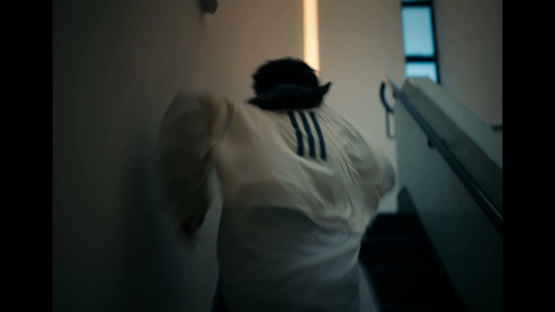 A person in a white jacket with black stripes on the back runs up a flight of stairs in a modern building.