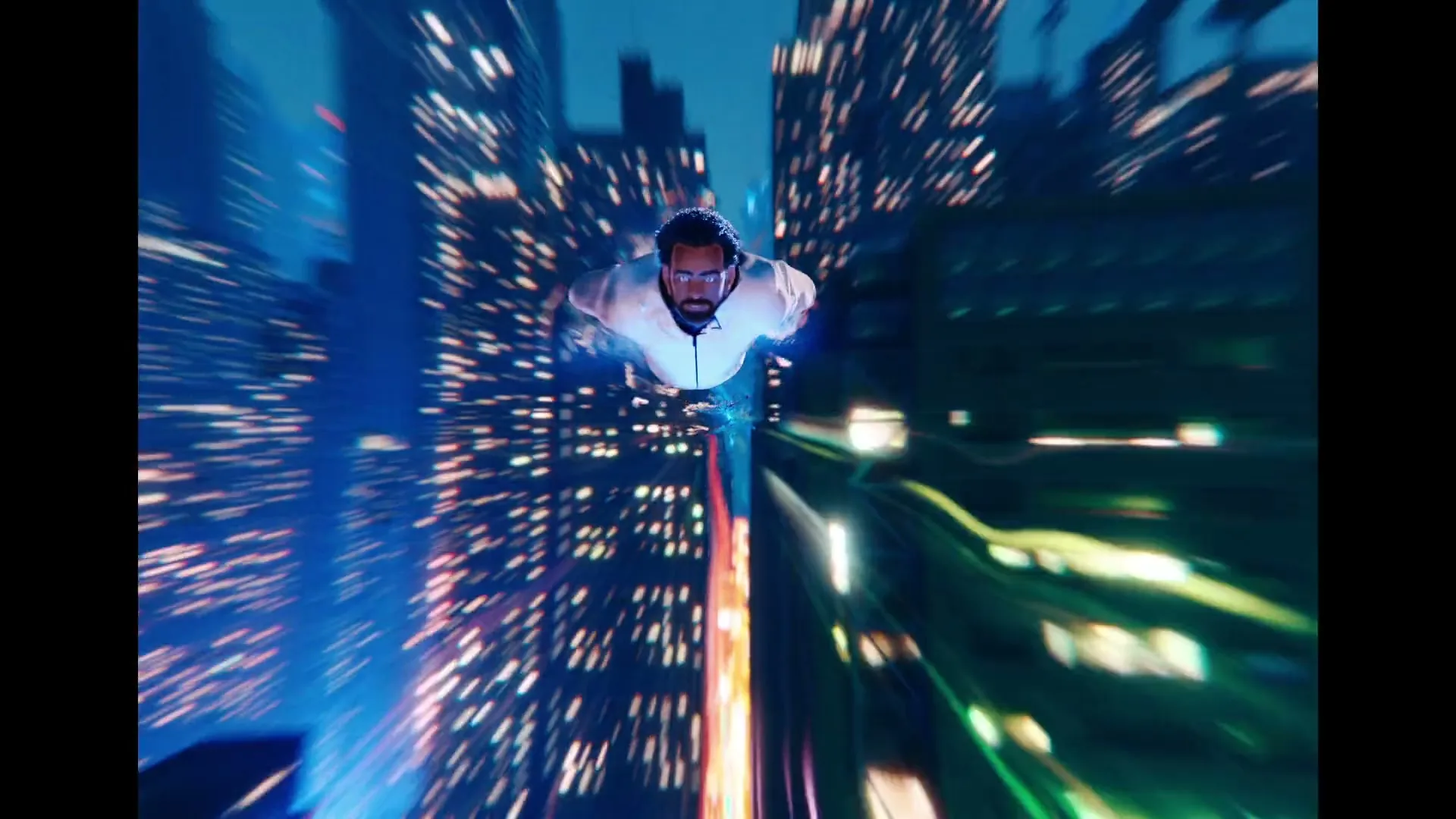 A man with a beard and glasses, wearing a white shirt, flies through a futuristic city at night, with blurred lights streaking past.