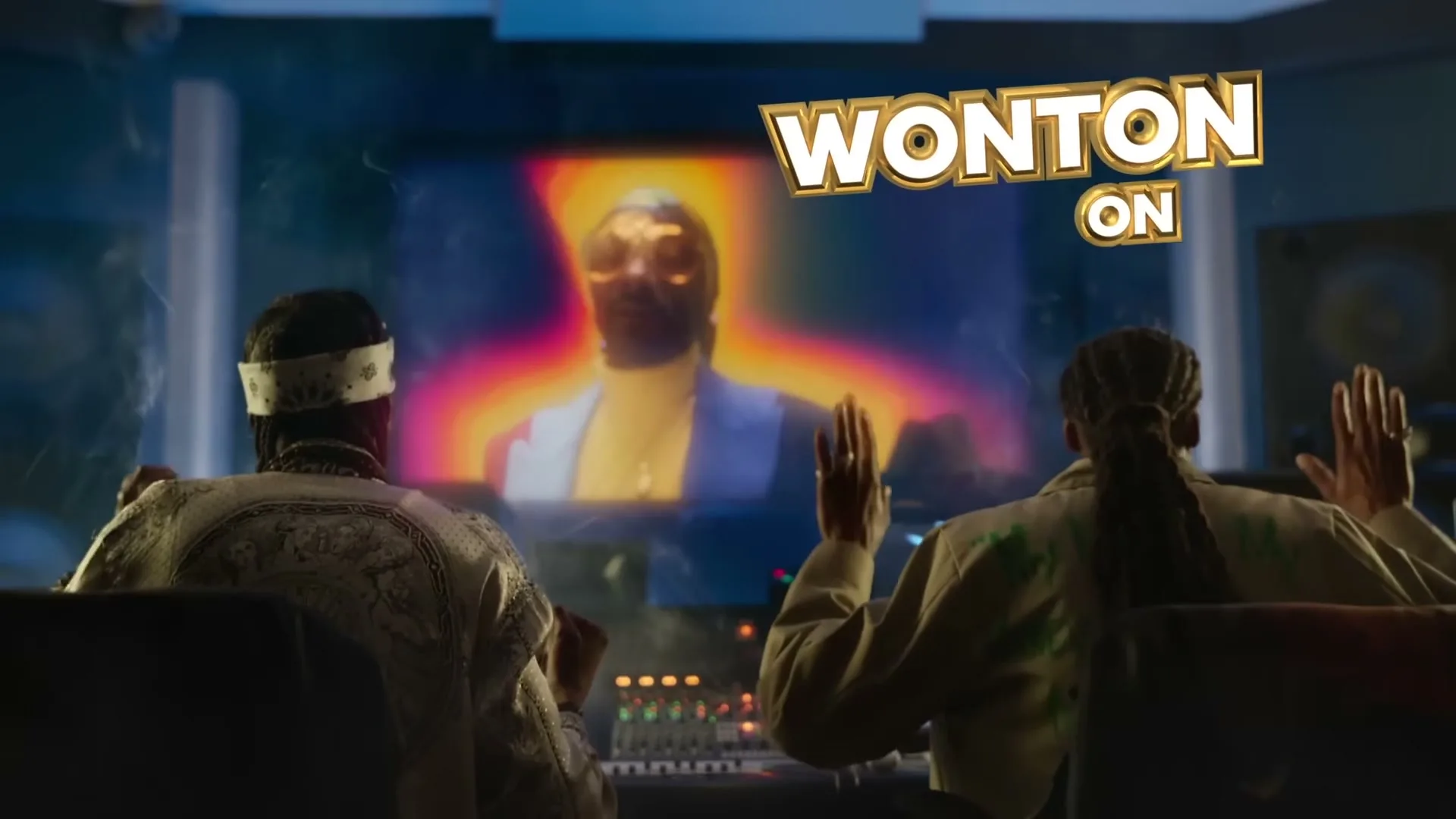 Two men in a recording studio watch Snoop Dogg on a screen, as text and a catamaran appear on screen.