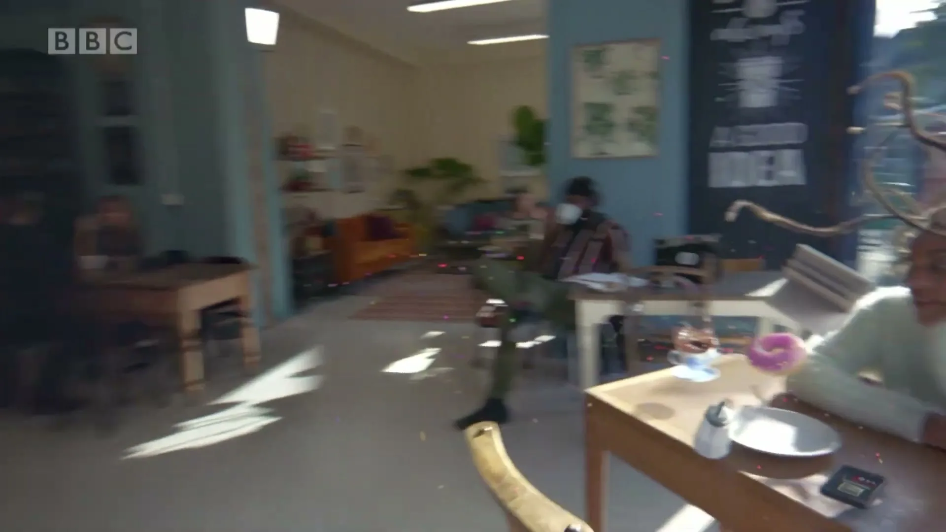 A diverse group of people in a cafe are affected by sound waves, causing them to float and their hair to become animated, as the camera moves through the space.