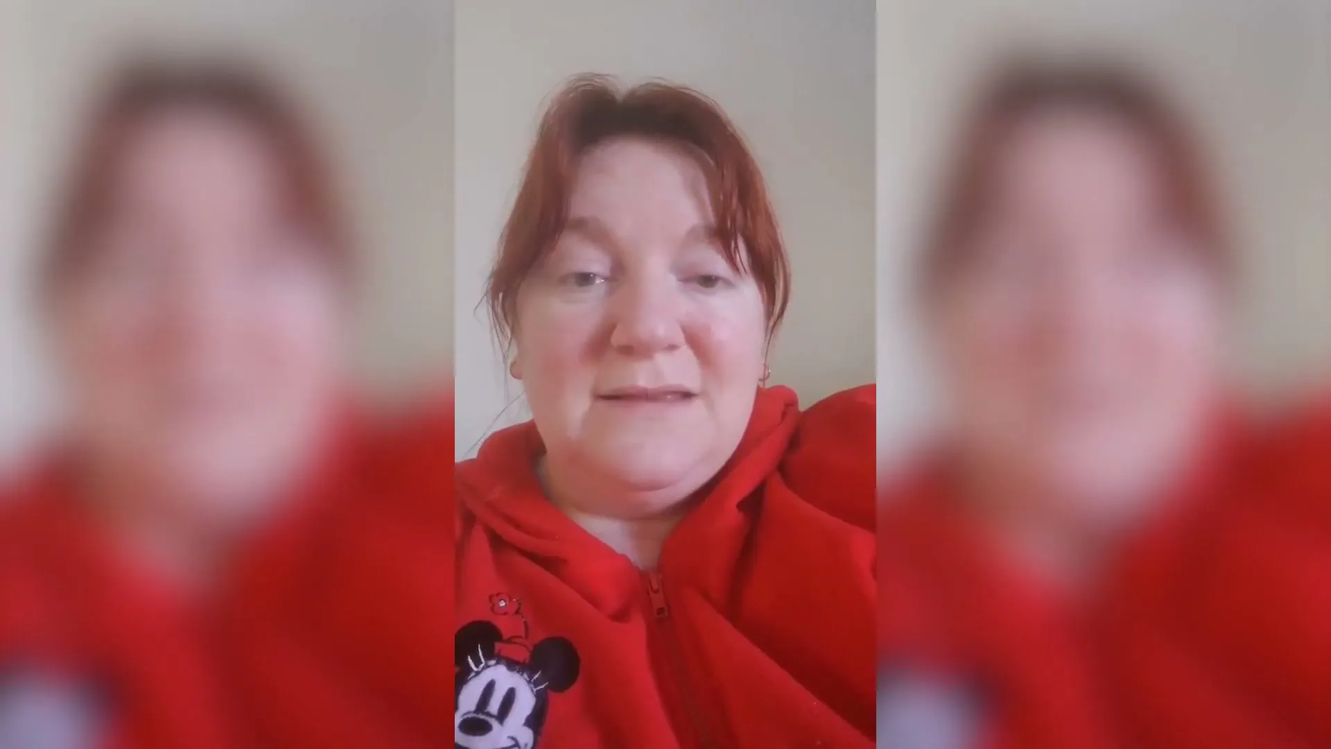 A woman with red hair and a red Mickey Mouse hoodie looks at the camera and talks in a medium shot.