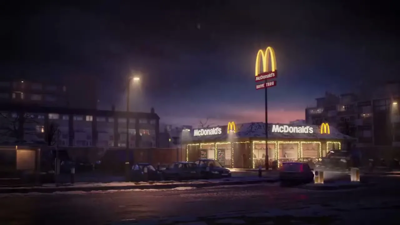 A wide shot of a McDonald's restaurant at night, decorated with Christmas lights, with cars parked outside and snow on the ground.