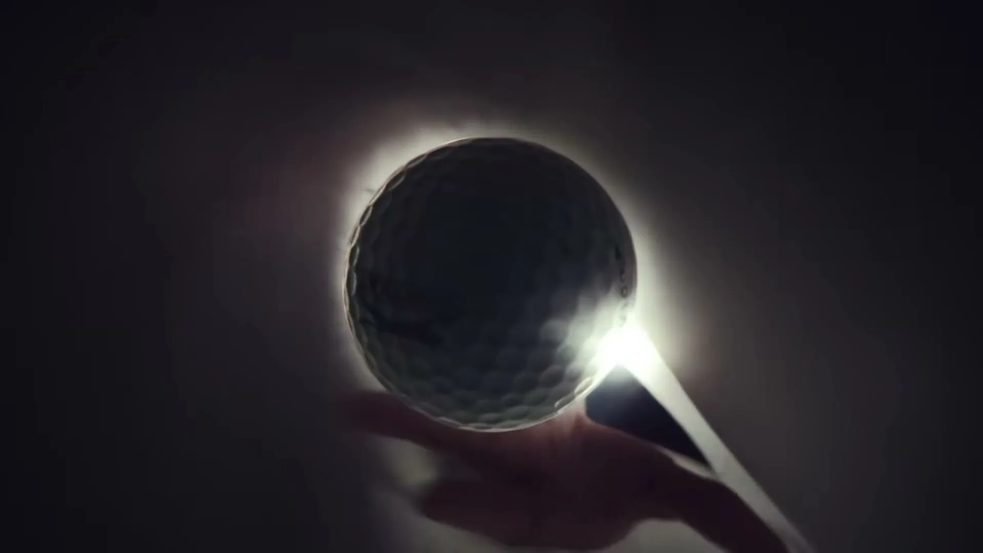 A golf ball is held in a hand, glowing brightly against a dark background, then placed into a white golf bag.
