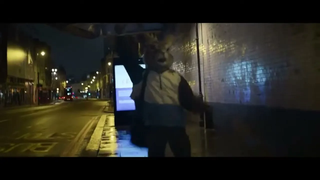 A person in a rabbit costume runs along a wet city street at night, illuminated by streetlights and reflections.