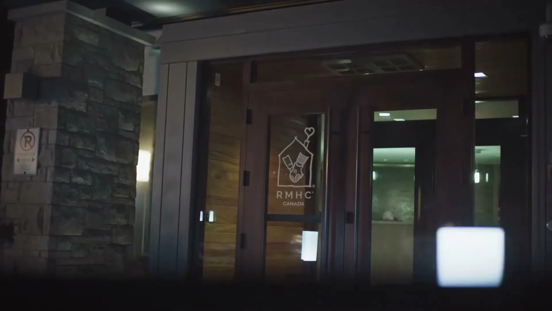 A wide shot of the entrance to a building at night, with the RMHC Canada logo visible on the glass doors.