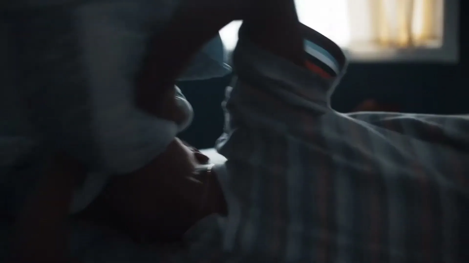 A child in pajamas lies in bed, covering their head with a pillow in a dimly lit bedroom.