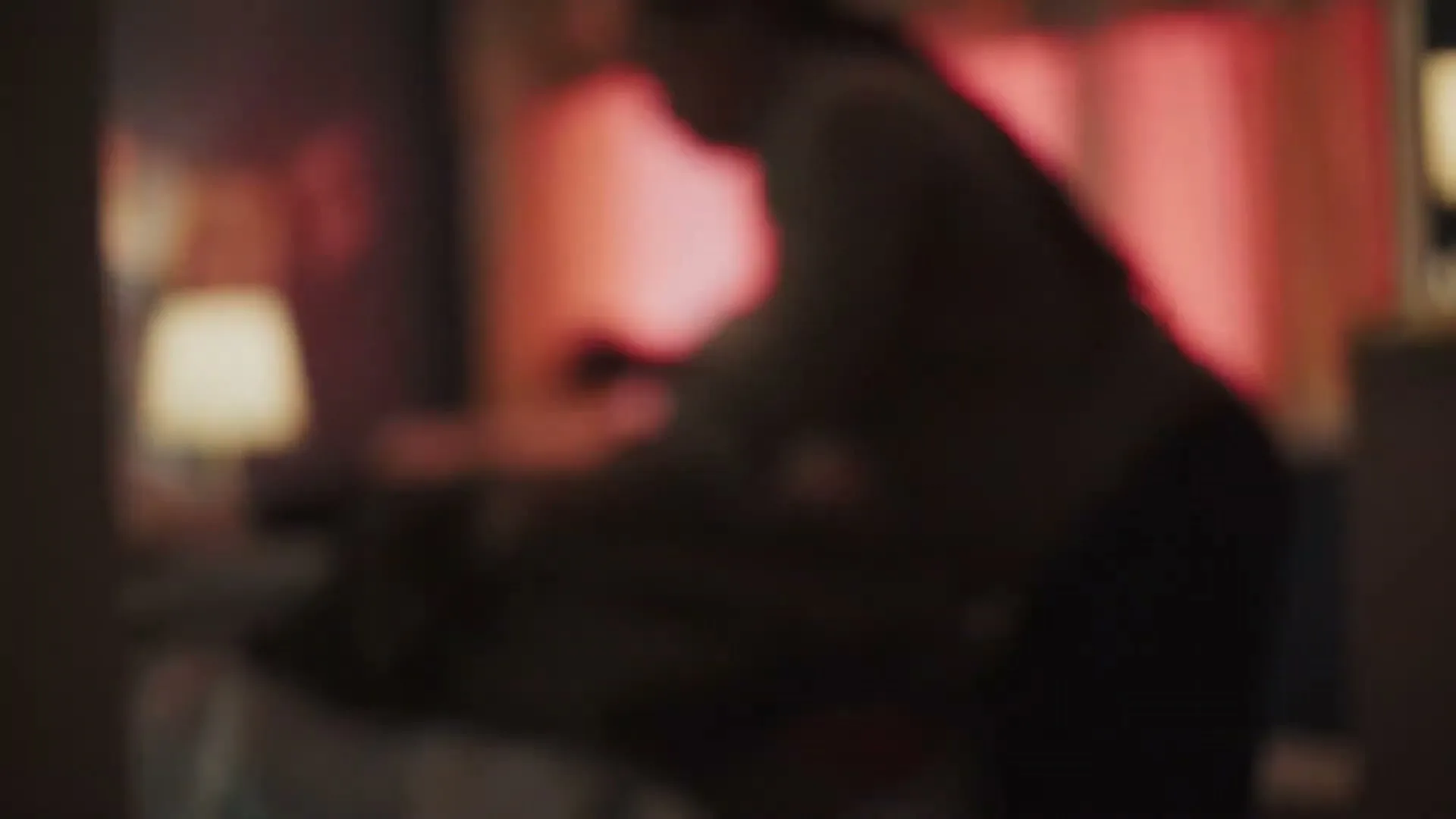 A blurry shot of a woman in a grey hoodie and a man in a blue shirt, tending to a child in a bed in a dimly lit bedroom.