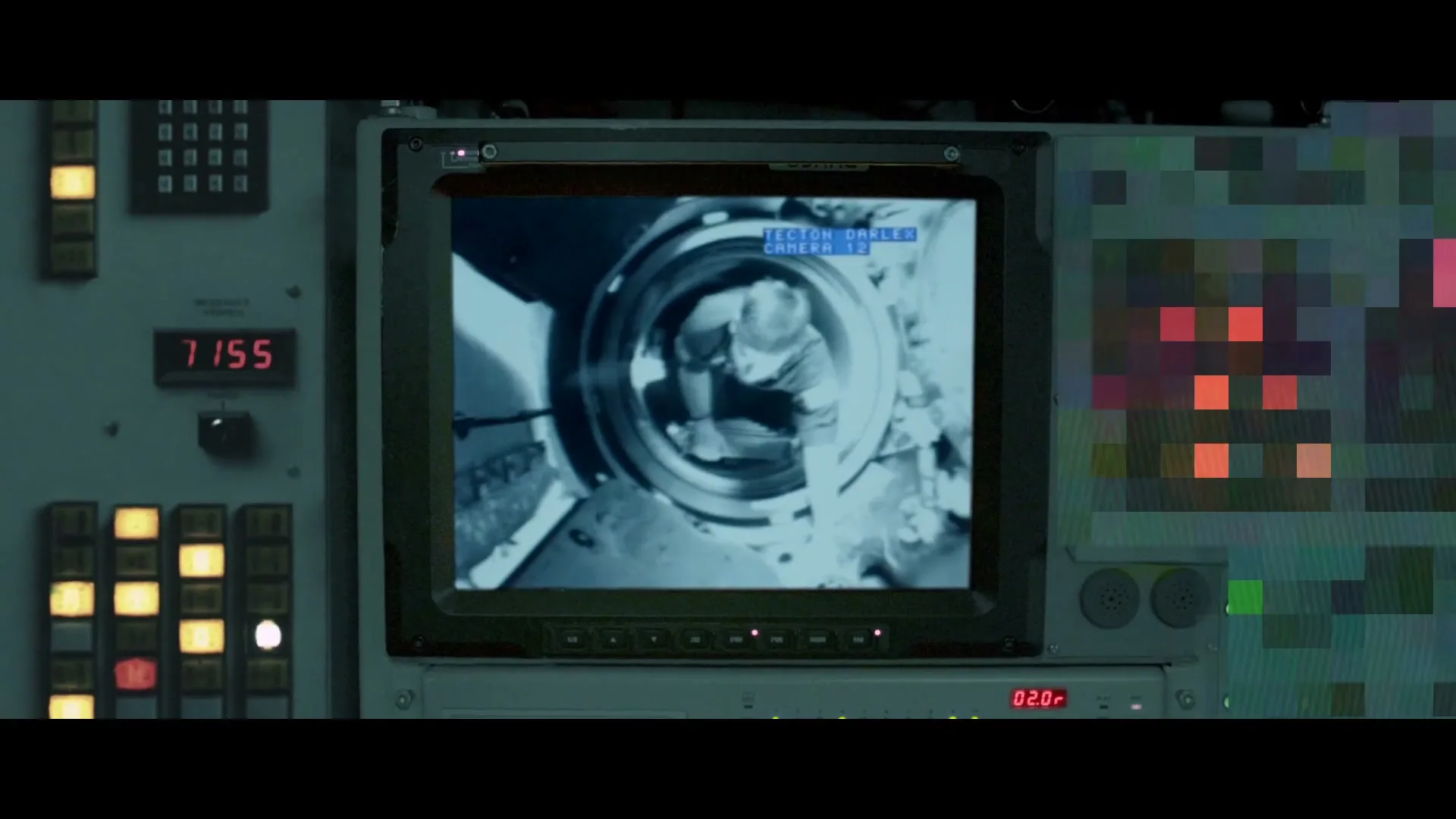 A man in a white shirt is seen through a circular monitor, reaching into a confined space, surrounded by control panels in a submarine.