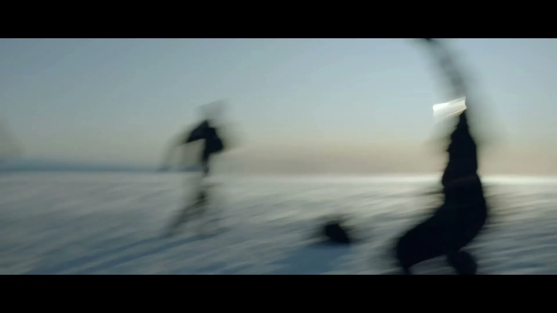 A group of people in winter clothing play soccer on a vast, snow-covered plain under a bright sky.