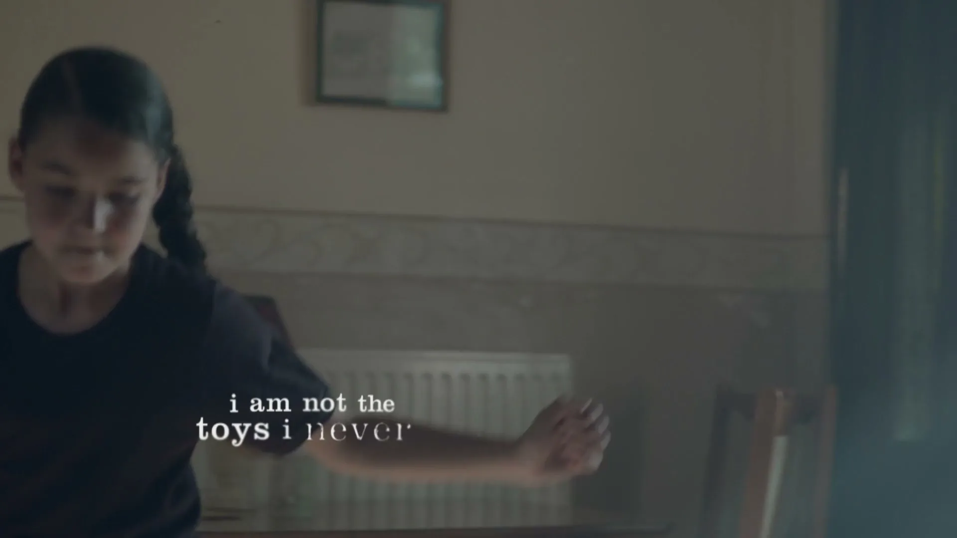 A young girl with dark hair in pigtails, wearing a dark t-shirt, juggles a football in a dimly lit room, with text overlay.