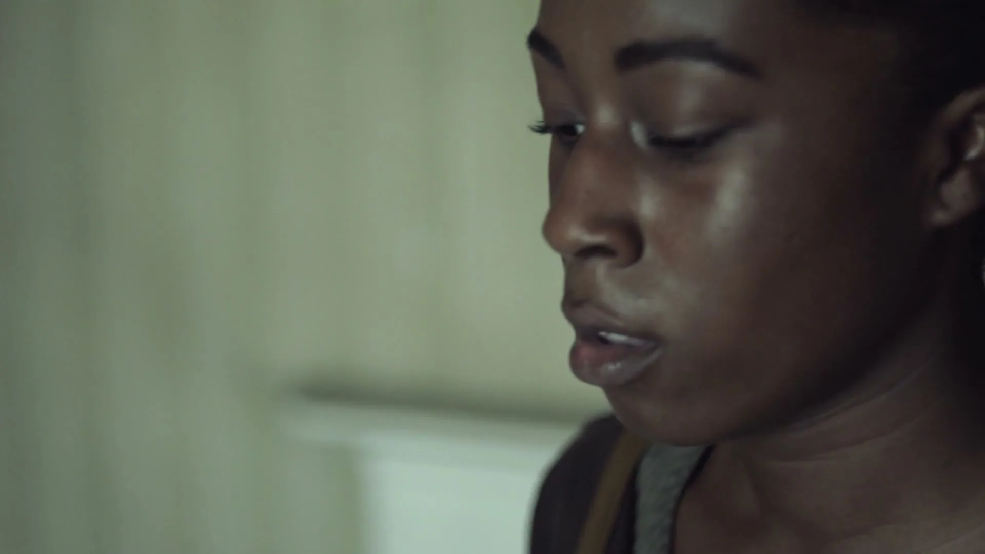 A young Black woman with dark hair and a grey top looks down and to the right, with text appearing on the left side of the screen.