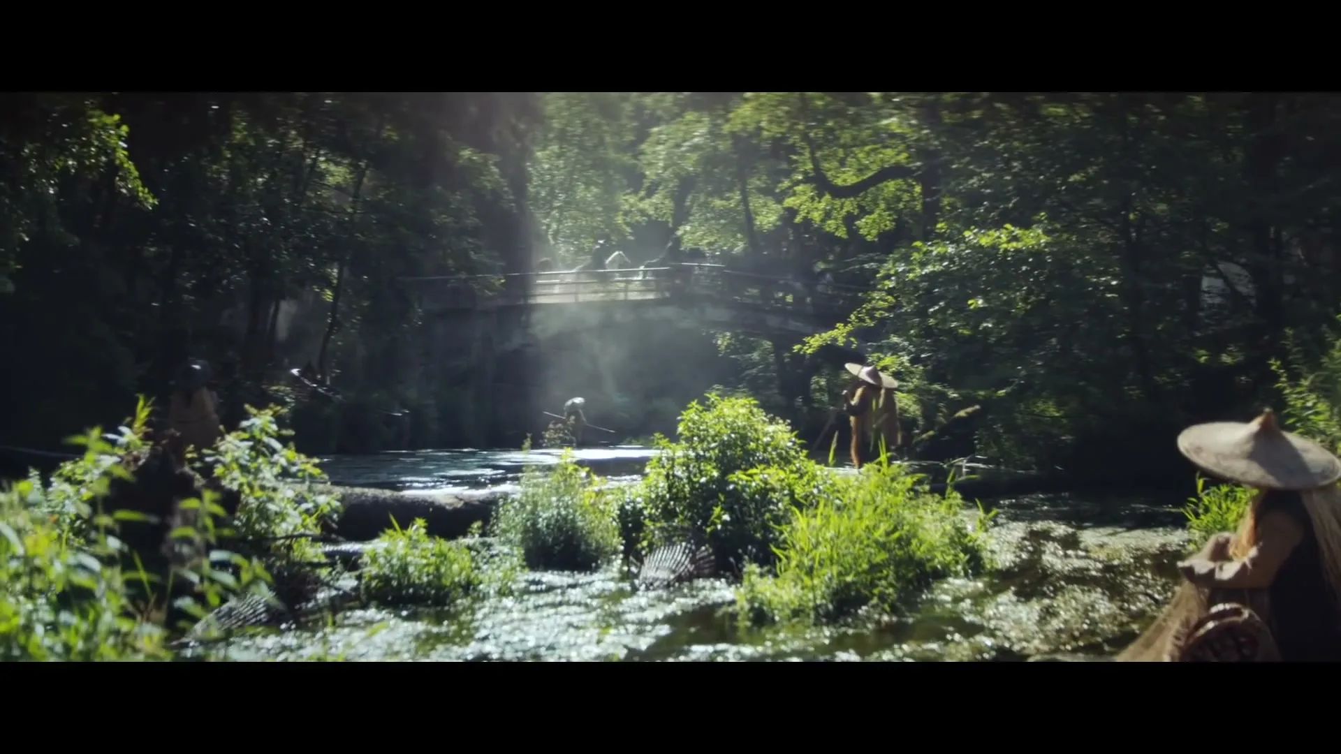 A group of people in traditional Asian attire are walking through a lush, green forest with a river and a stone bridge in the background.