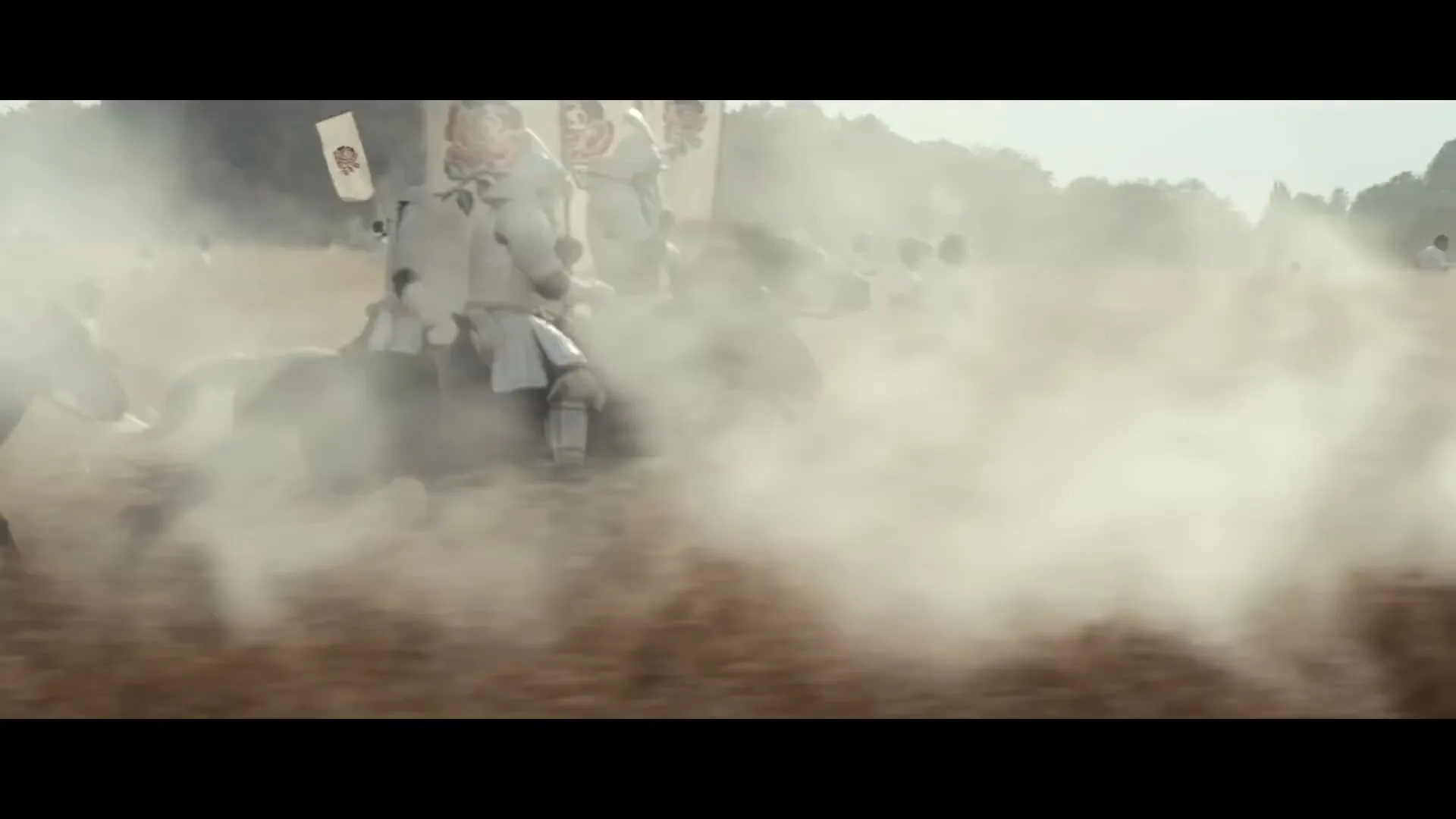 Armored knights on horseback charge through a dusty field, carrying banners with red roses, as other people in white shirts run in the background.