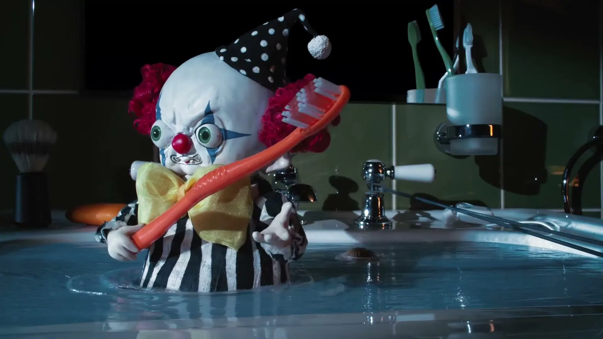A stop-motion clown puppet with a polka-dot hat and red hair holds a giant toothbrush while standing in a bathtub in a bathroom.