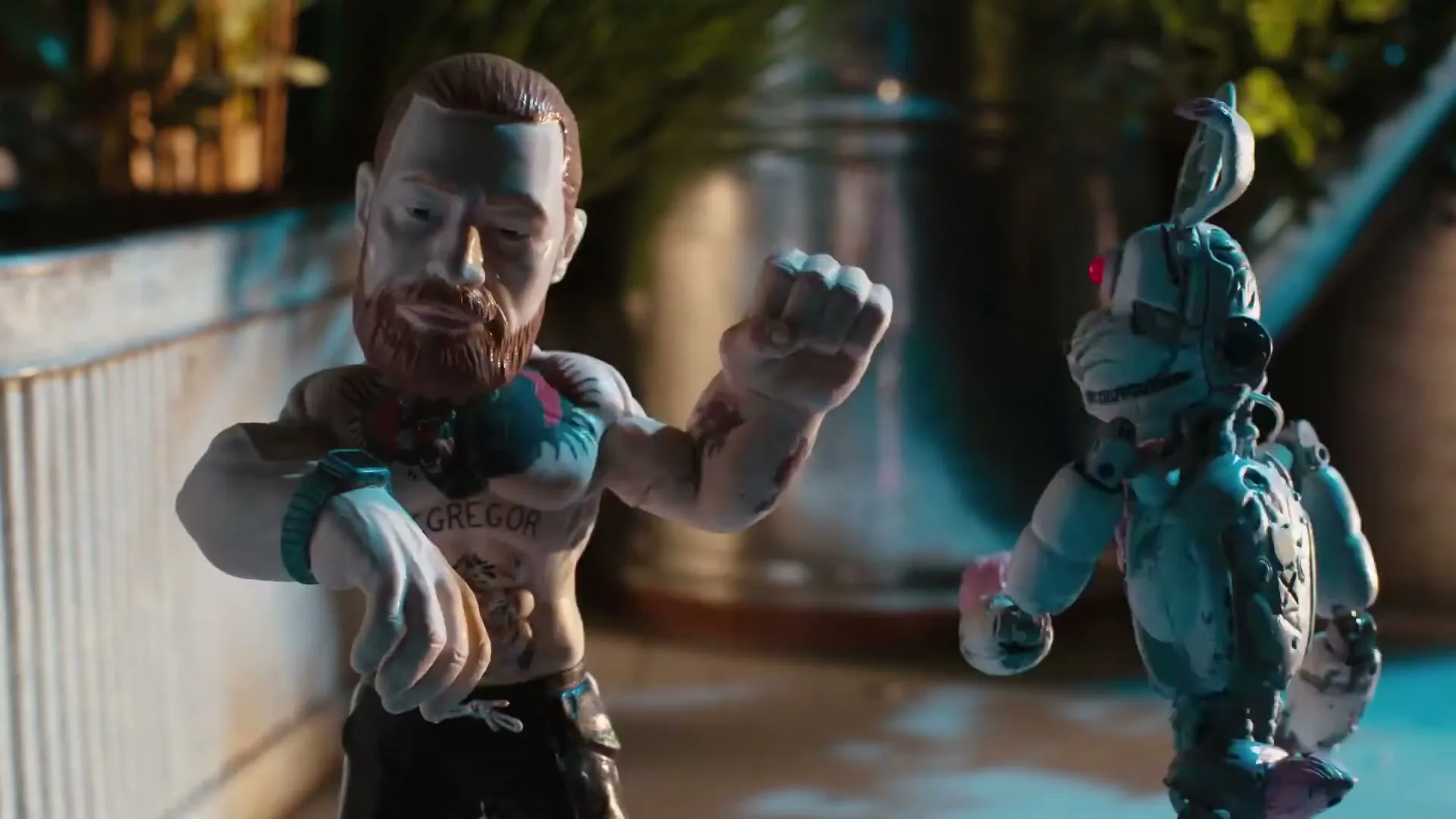 A bobblehead-like figurine of Conor McGregor, with tattoos and a beard, is shown in a medium shot, then a robot-like figurine appears and they interact.
