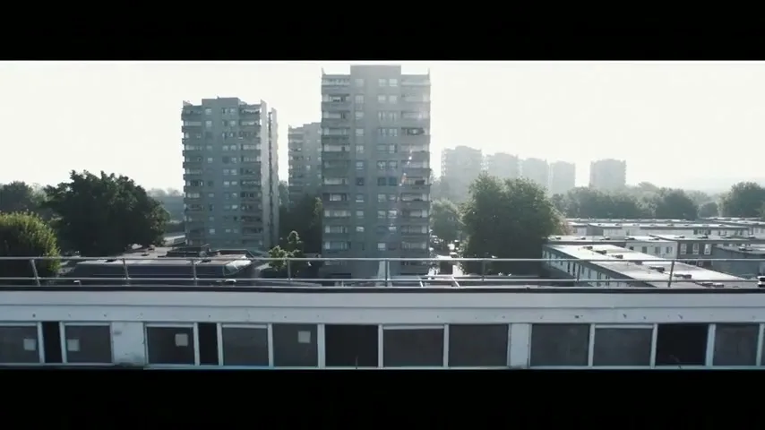 An aerial shot of a city with tall buildings and trees, with a bright sky in the background, as the camera slowly pans down.
