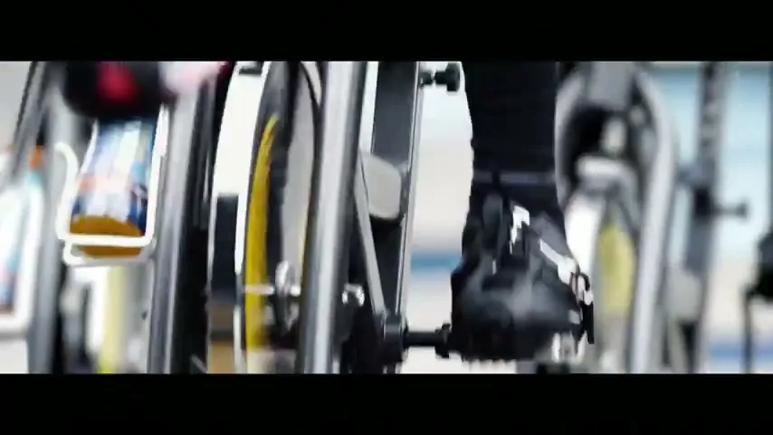 A person's feet in athletic shoes pedal a stationary bike in a gym, with other bikes blurred in the background.