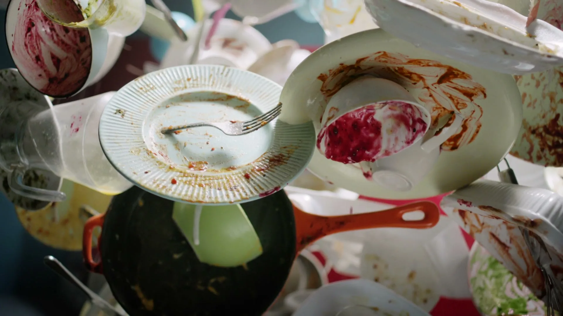A pile of dirty dishes, including plates, bowls, and cups, with food residue, is shown in a close-up shot.