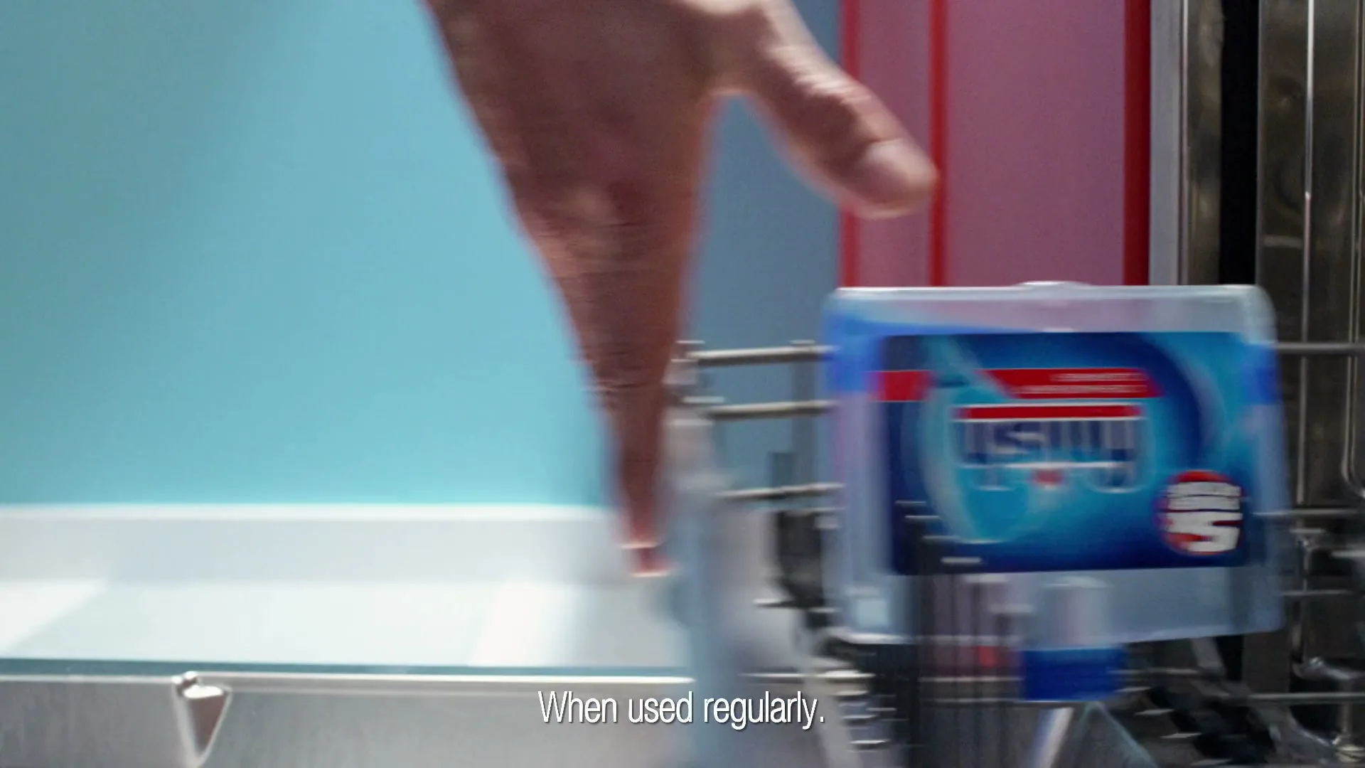 A hand places a Finish dishwasher cleaner bottle into the top rack of a dishwasher in a kitchen.