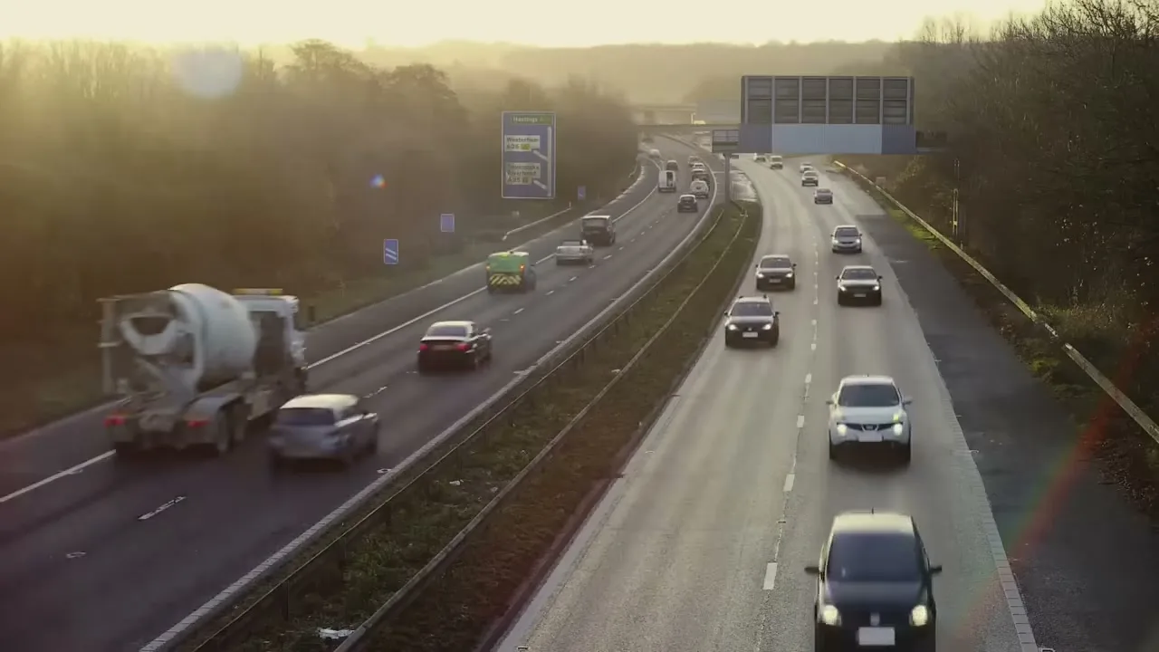 An aerial shot of a multi-lane highway with cars driving in both directions, surrounded by trees under a bright sky.