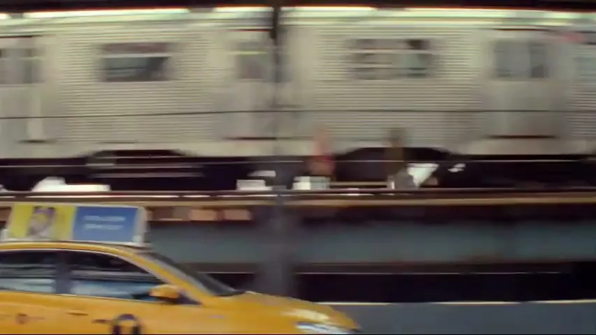 A yellow taxi cab drives past an elevated train as it moves along the tracks in a city.
