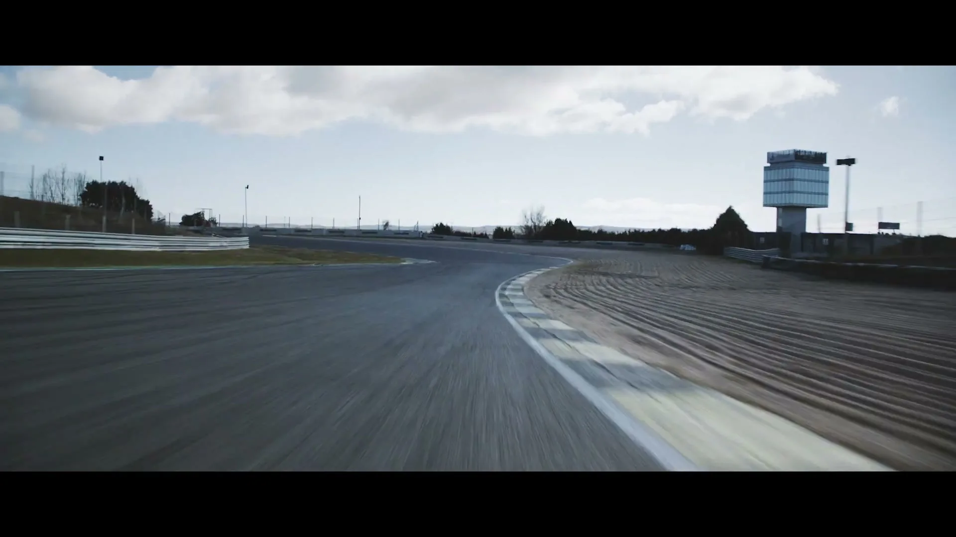 A wide shot of an empty race track with a control tower in the background under a cloudy sky.
