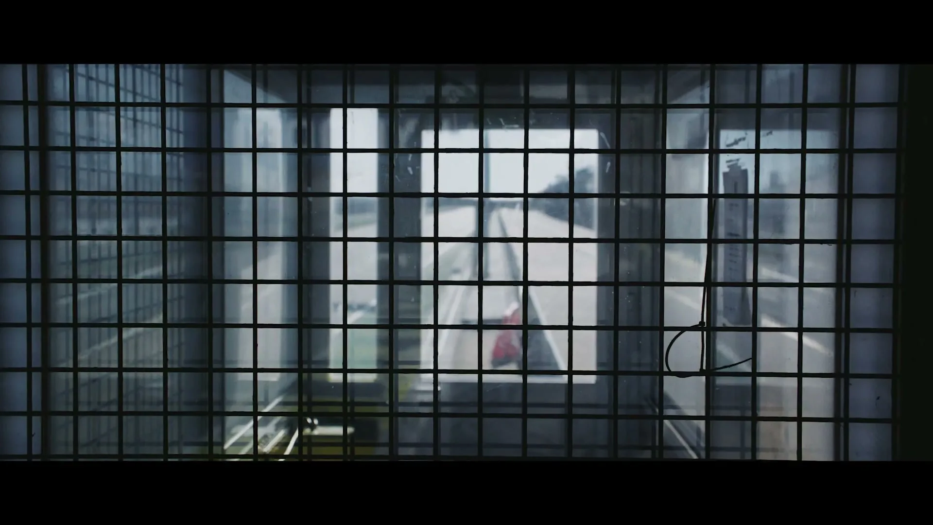 A wide shot of a race track seen through a metal grid, with a red and white barrier visible in the distance.