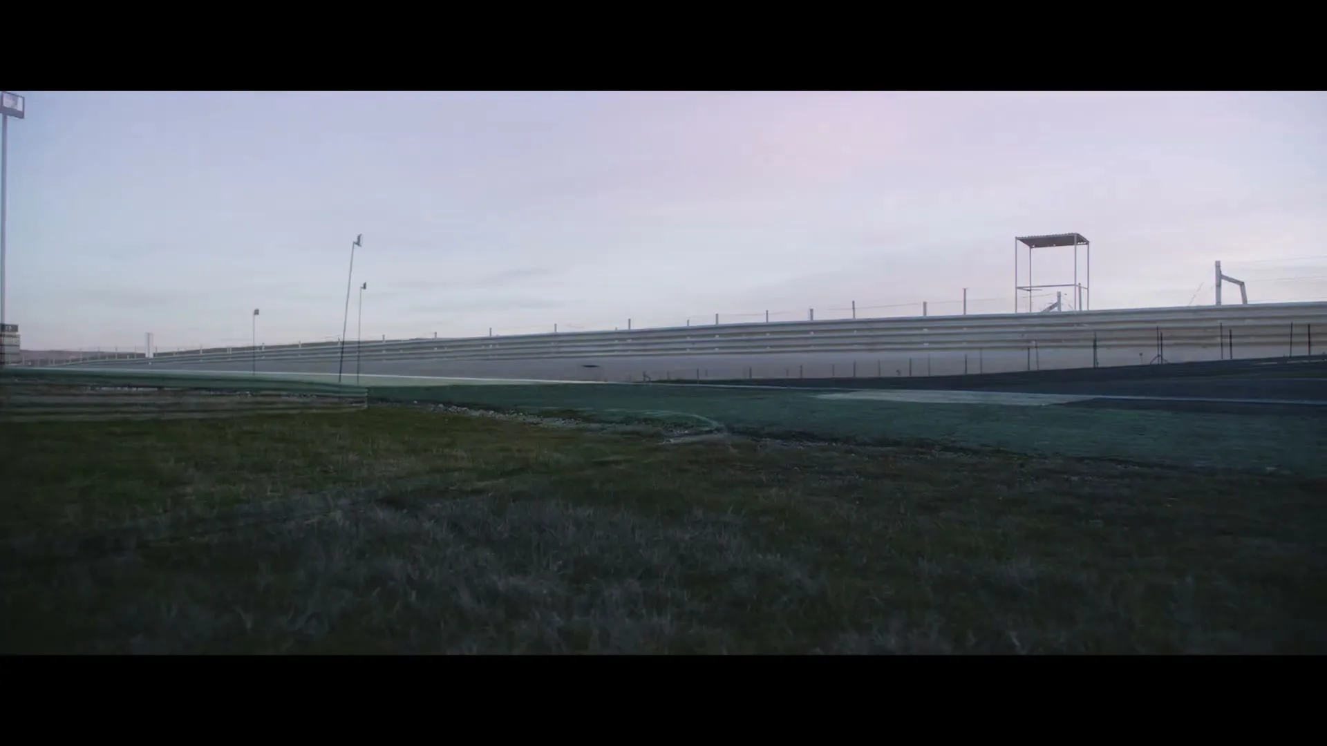 A white race car speeds along a track at dawn, with a subtle double exposure of a garage door and a person in a helmet.